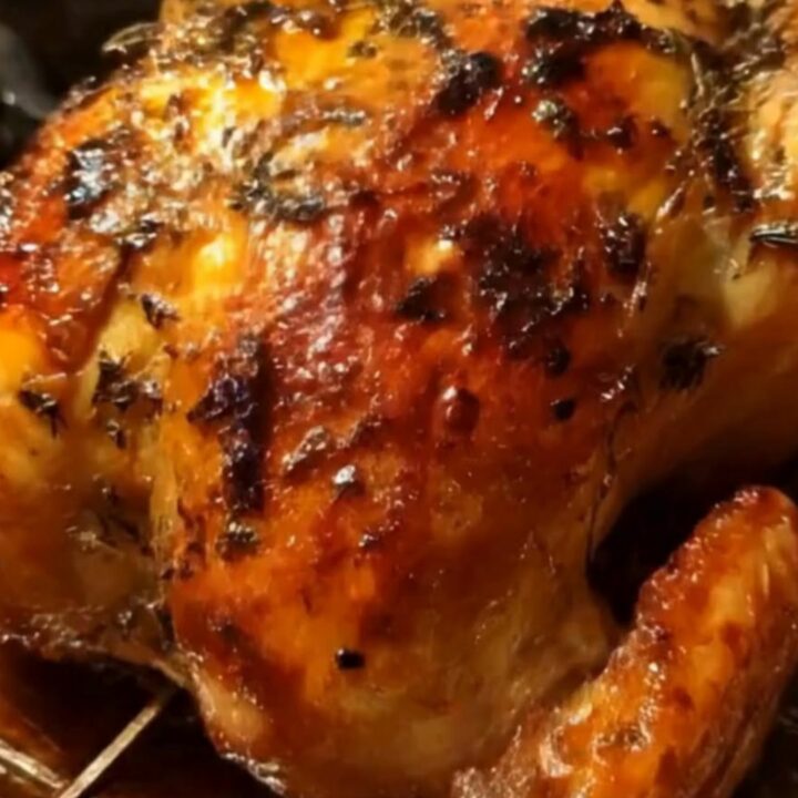 A whole golden-brown roasted chicken resting on a wire rack with blistered, ultra-crispy skin in warm kitchen lighting.