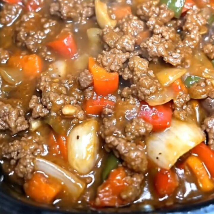 A slow cooker filled with steaming, glossy pepper steak made with ground beef and colorful bell peppers.