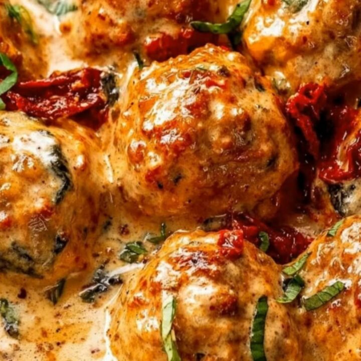 A smooth push-in shot of glistening golden chicken meatballs in a thick, specked cream sauce garnished with fresh basil