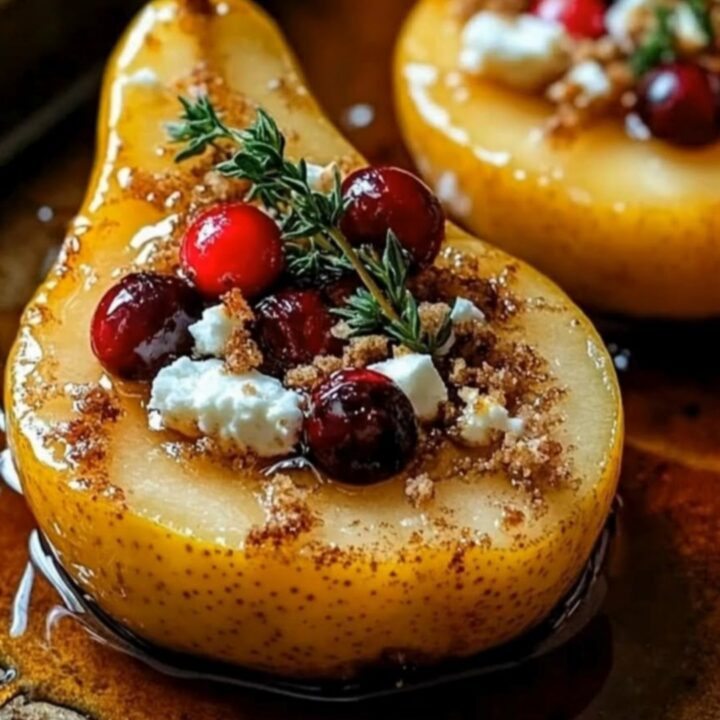 A beautiful close-up of roasted holiday pear halves topped with sparkling red cranberries, crumbled feta, and fresh thyme