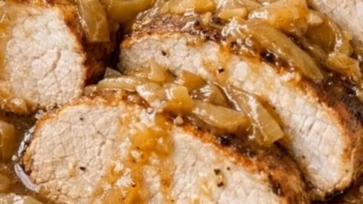 A white ceramic baking dish filled with juicy sliced pork tenderloin medallions smothered in glossy caramelized onion gravy.