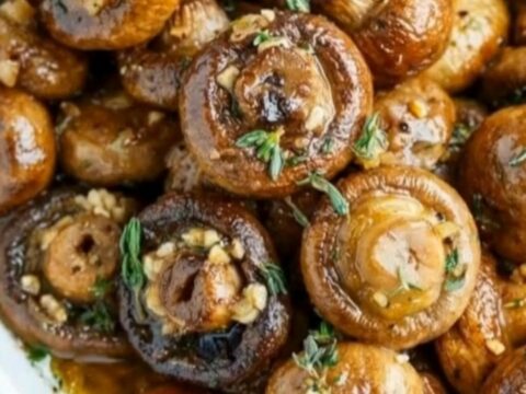 A white oval baking dish filled with juicy, golden-brown garlic butter mushrooms garnished with fresh thyme.