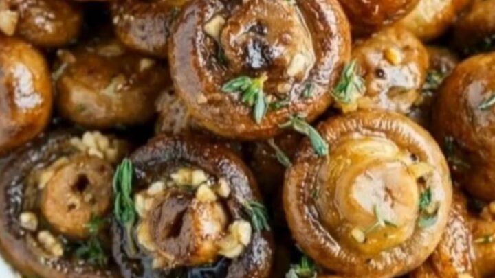 A white oval baking dish filled with juicy, golden-brown garlic butter mushrooms garnished with fresh thyme.