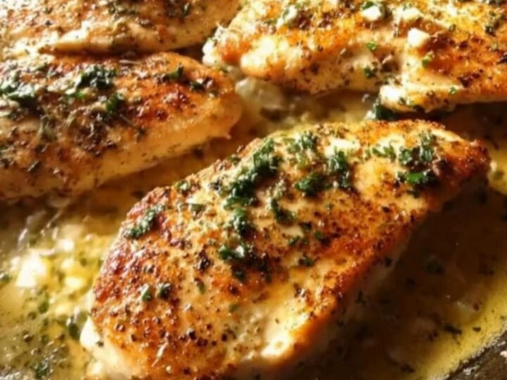Five golden-brown chicken breasts simmering in a rich garlic butter sauce garnished with fresh parsley in a cast iron