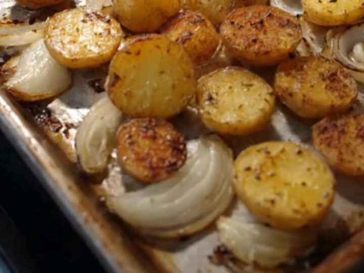 A rustic sheet pan filled with golden, crispy halved baby potatoes and sweet caramelized onion wedges.
