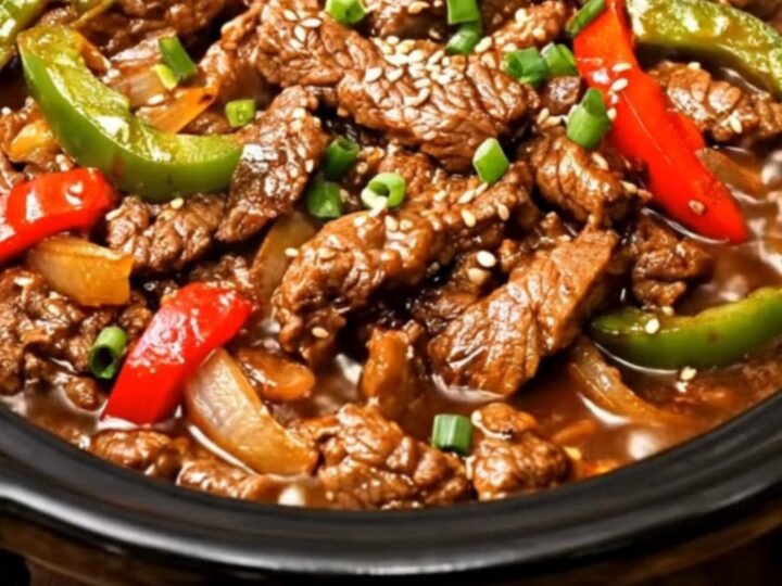 A close-up of tender beef strips and vibrant bell peppers in a glossy brown sauce inside a slow cooker.
