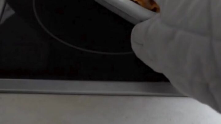 A spatula lifting a cheesy baked lasagna roll from a white ceramic baking dish with a long mozzarella cheese pull.