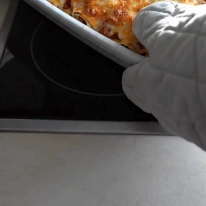 A spatula lifting a cheesy baked lasagna roll from a white ceramic baking dish with a long mozzarella cheese pull.