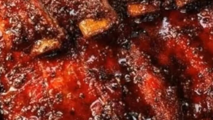 A rack of tender, glazed pork ribs being pulled apart, revealing juicy meat and glistening sticky sauce.