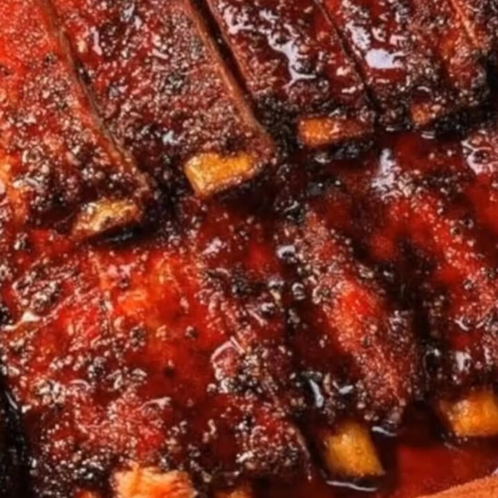 A rack of tender, glazed pork ribs being pulled apart, revealing juicy meat and glistening sticky sauce.