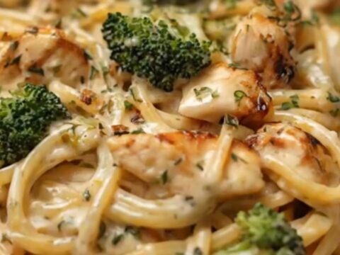A fluted white bowl filled with creamy Alfredo chicken linguine and vibrant green broccoli under warm lights