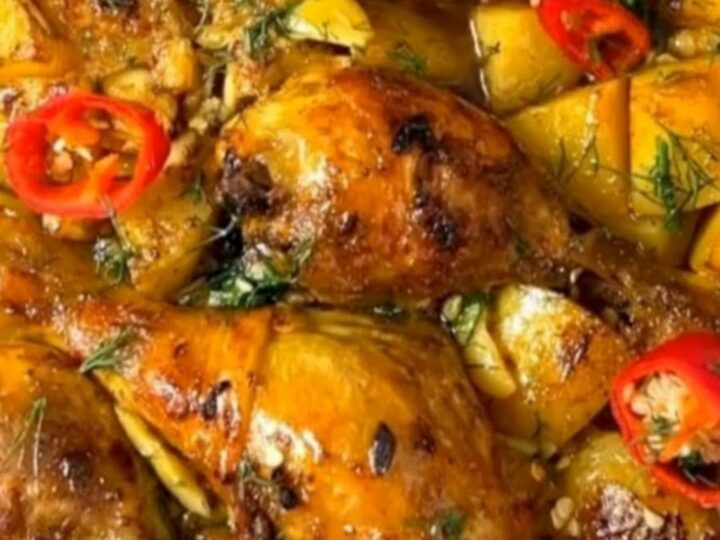 A ceramic baking dish filled with golden, crispy garlic roasted chicken drumsticks and tender potato wedges