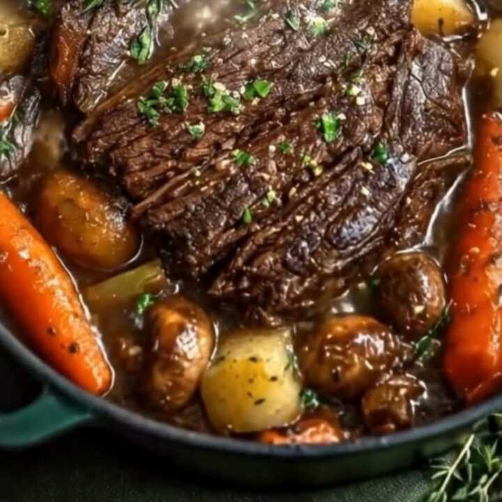 A dark Dutch oven containing sliced, tender beef pot roast surrounded by glistening glazed carrots and mushrooms