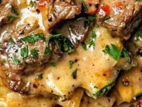 A plate of creamy steak spaghetti with zucchini, garnished with parsley flakes in warm cinematic lighting.