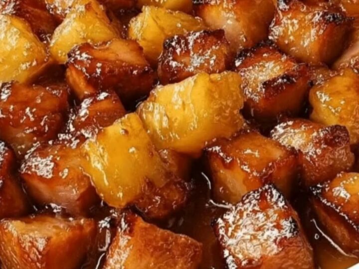 A white oval baking dish filled with sticky, caramelized ham cubes and golden pineapple chunks under warm lighting.