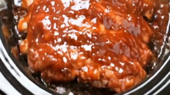 A rack of glossy, saucy crockpot BBQ ribs resting in a black oval slow cooker, looking extremely tender and delicious.
