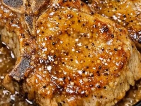 A succulent bone-in pork chop glazed with sticky honey garlic sauce, sliced open to reveal juicy meat inside.