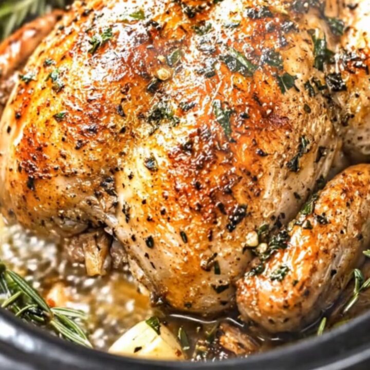 A golden, glistening slow cooker rotisserie chicken garnished with fresh rosemary sprigs and garlic cloves.