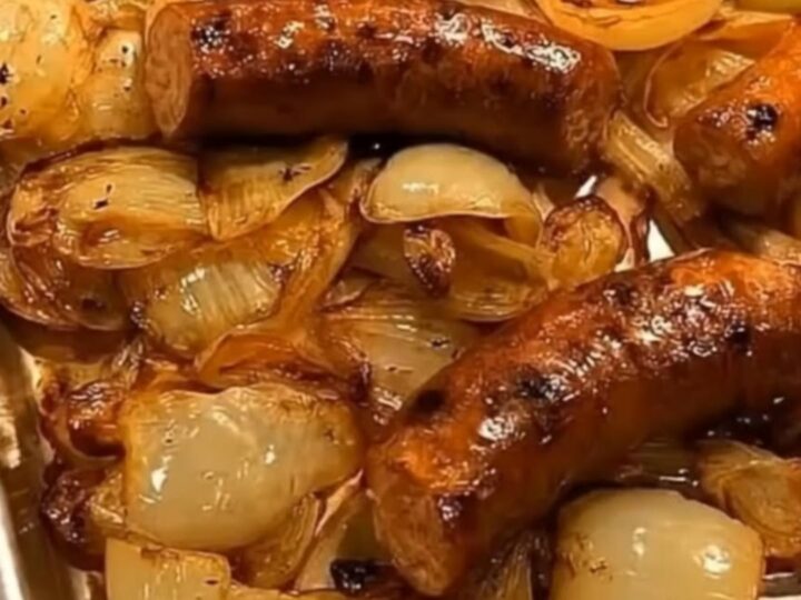 A metal sheet pan filled with roasted sausages nestled in a bed of tender, caramelized golden onions