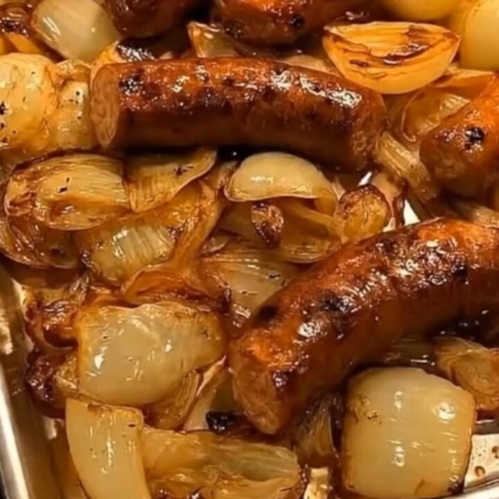 A metal sheet pan filled with roasted sausages nestled in a bed of tender, caramelized golden onions