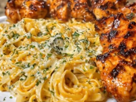 A steaming plate of creamy Cajun linguine garnished with fresh parsley next to sliced, charred Cajun chicken breasts.