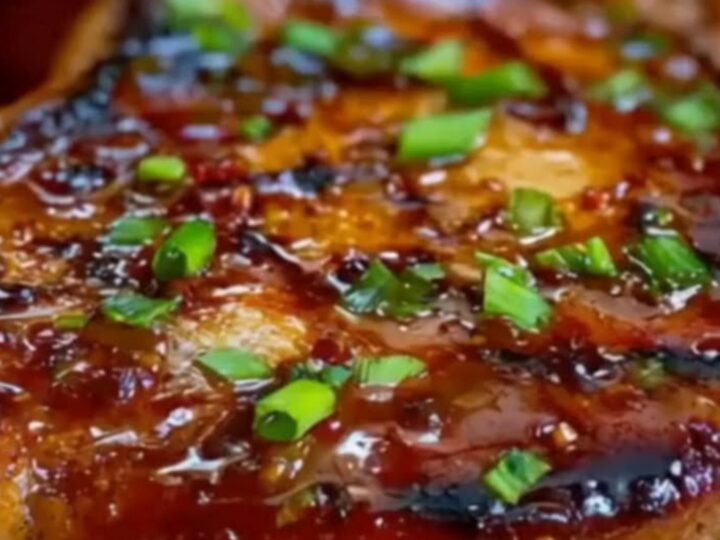 A glistening peach glazed pork chop served with caramelized roasted peach slices and sprinkled with green scallions