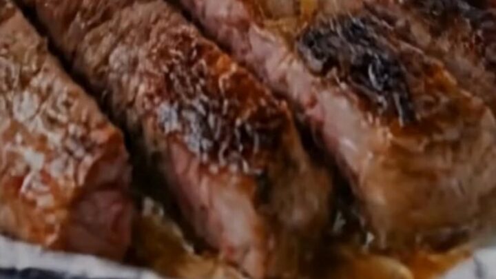 Sliced medium-rare garlic butter steak served next to golden roasted potatoes and onions in a foil-lined dish.