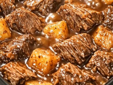 A black slow cooker filled with glistening beef cubes and tender potatoes in a rich, dark gravy