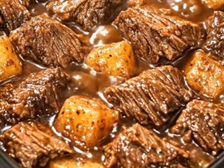 A black slow cooker filled with glistening beef cubes and tender potatoes in a rich, dark gravy