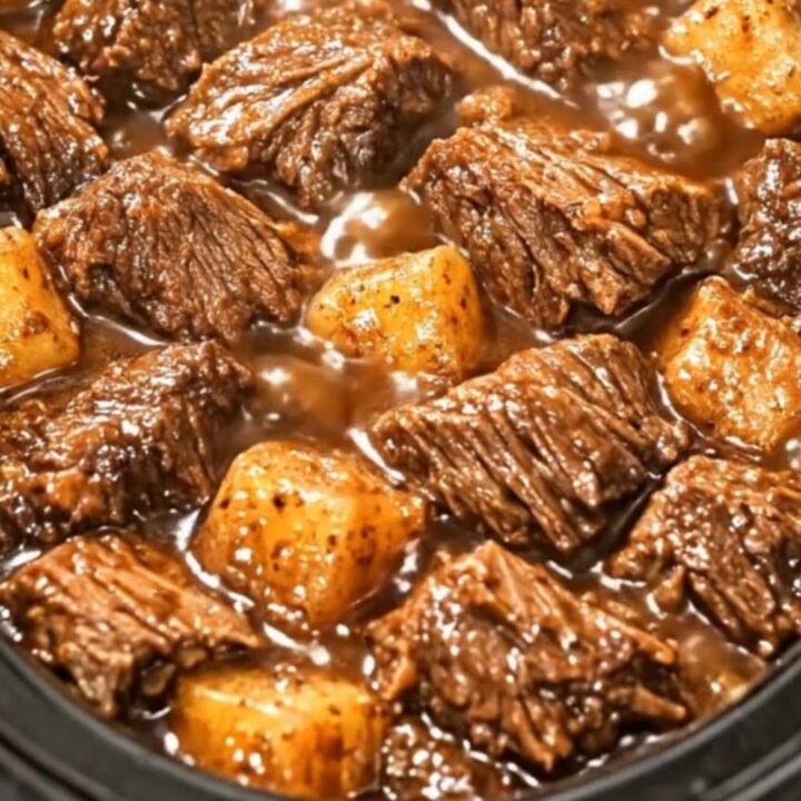 A black slow cooker filled with glistening beef cubes and tender potatoes in a rich, dark gravy
