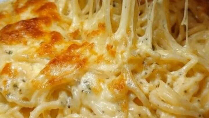 A plate of golden-baked cheesy garlic spaghetti with long melted cheese strands extending upwards