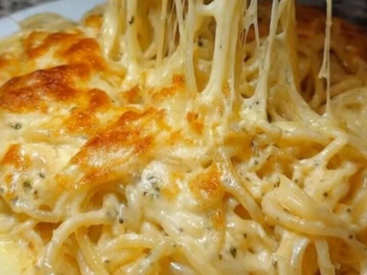 A plate of golden-baked cheesy garlic spaghetti with long melted cheese strands extending upwards