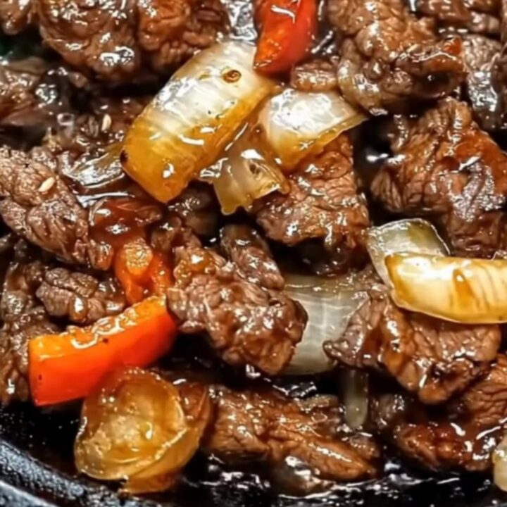 Sizzling Chinese pepper steak with glistening beef strips, translucent onions, and red peppers on a steaming black skillet.