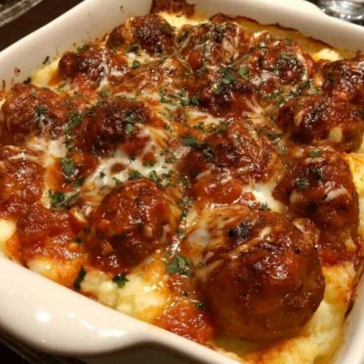 A bubbling casserole dish of cheesy meatball and mashed potato bake garnished with fresh parsley on a wooden table.
