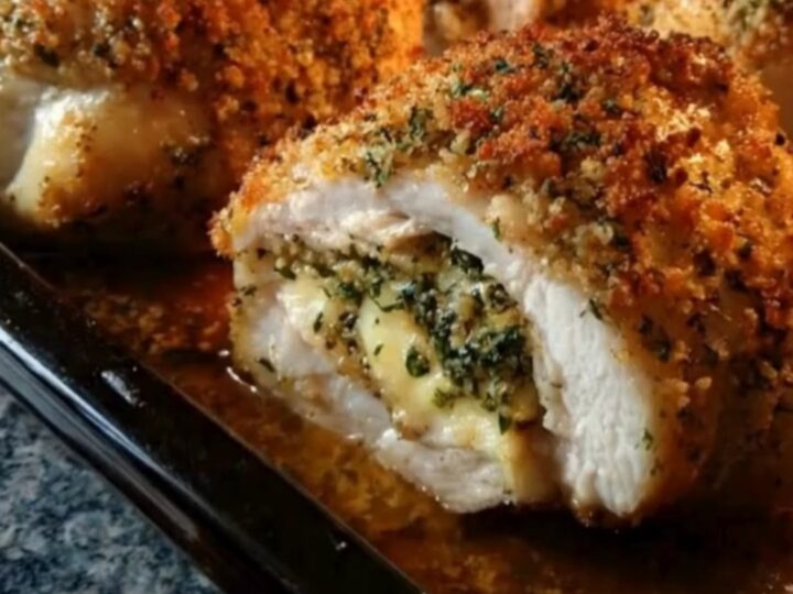 A golden brown baked stuffed chicken breast sliced open on a dark board, showing melted cheese oozing out