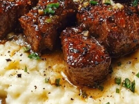 Tender garlic butter steak bites piled high over a bed of creamy mashed potatoes in a white shallow bowl