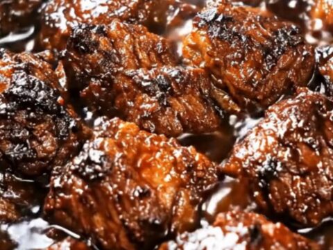 A close-up shot of caramelized, tender country-style boneless pork ribs simmering in a slow cooker.
