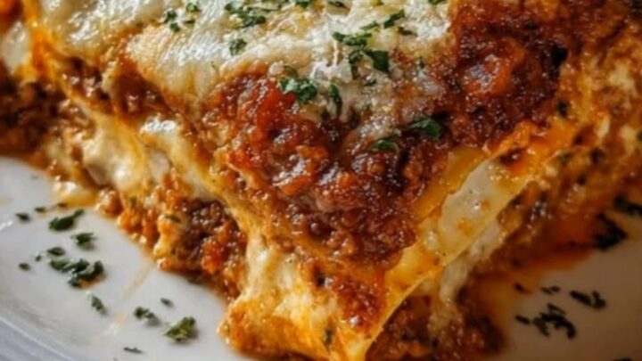 A close-up shot of a fork lifting a slice of cheesy meat lasagna, showing a long, stretchy cheese pull.