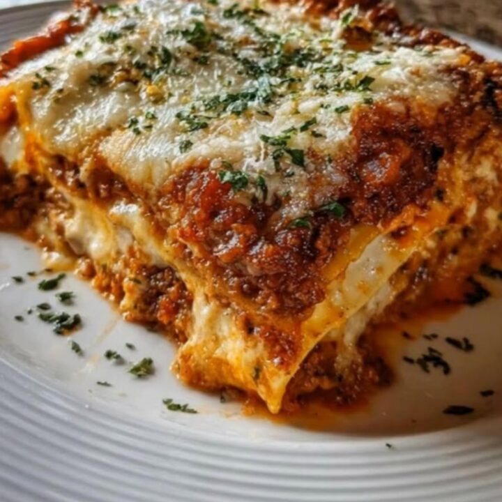 A close-up shot of a fork lifting a slice of cheesy meat lasagna, showing a long, stretchy cheese pull.