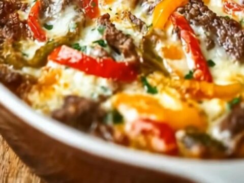 A bubbly cheesy beef and pepper bake in a white baking dish on a rustic wooden table with rising steam.