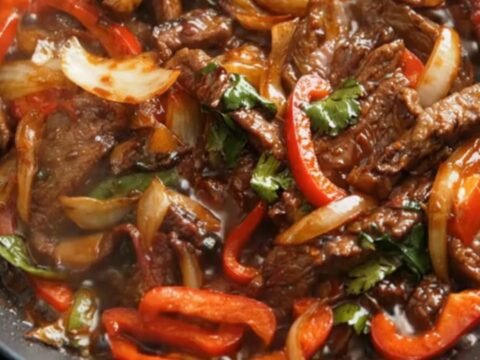 A hot skillet filled with glistening, tender beef strips and vibrant red bell peppers in a rich brown sauce
