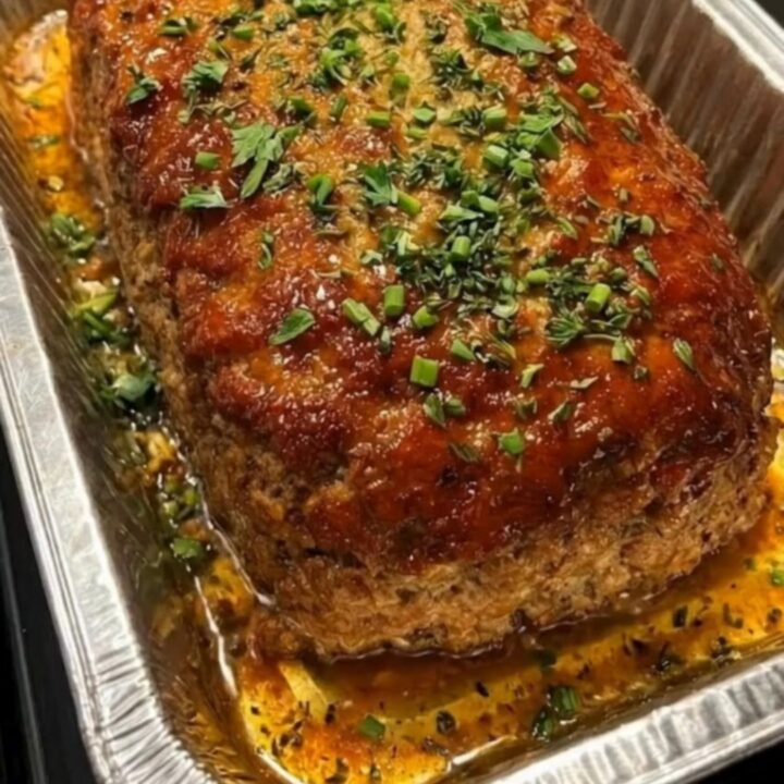 A close-up shot of a sliced sweet glazed meatloaf topped with a shiny mahogany glaze and fresh parsley