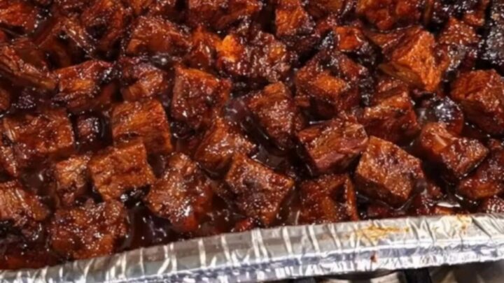 A disposable foil pan filled with glistening, caramelized poor man's burnt ends coated in a sticky glaze.