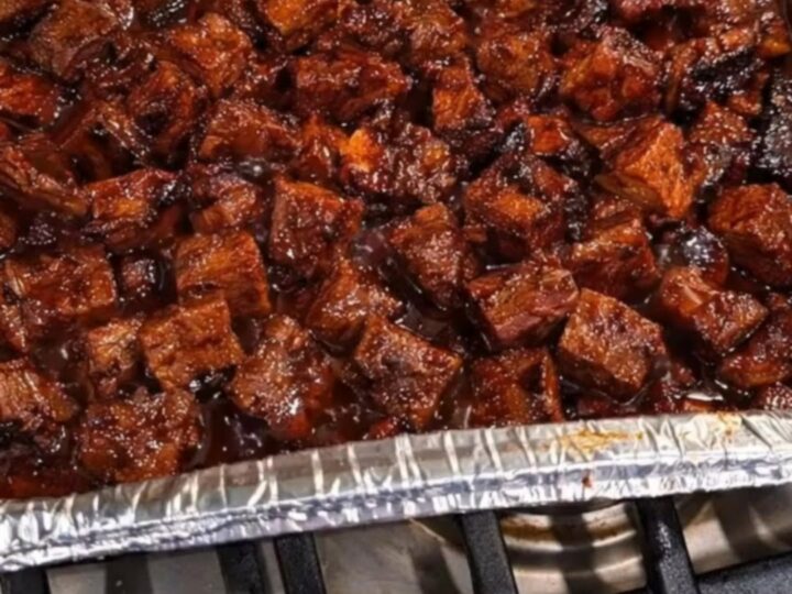 A disposable foil pan filled with glistening, caramelized poor man's burnt ends coated in a sticky glaze.
