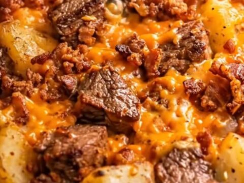 A slow cooker filled with tender seared steak, golden cubed potatoes, melted cheddar cheese, and crispy bacon.