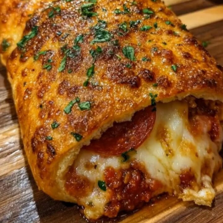 A golden brown pepperoni pizza stromboli sliced on a wooden board with marinara dipping sauce.
