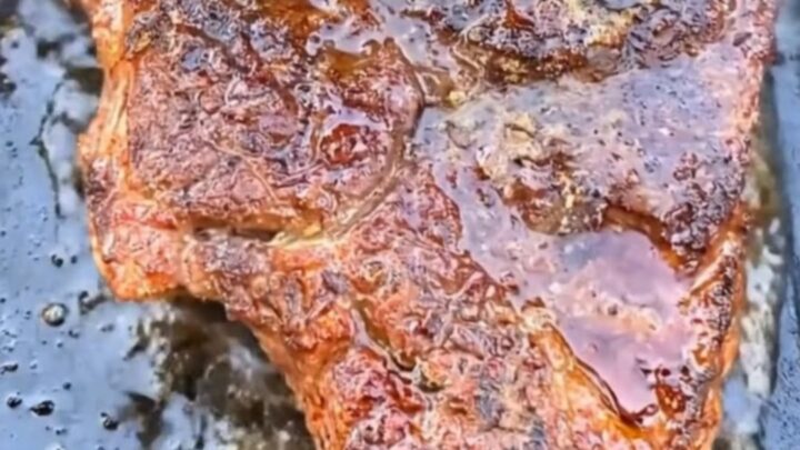 A beautifully seared ribeye steak resting on a hot griddle, glistening with melted garlic herb butter.