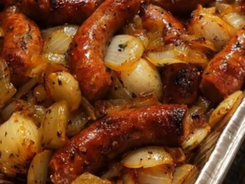 A sizzling aluminum foil pan filled with plump, charred Italian sausage links and sweet caramelized onions.