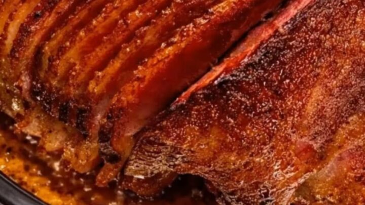 A beautifully caramelized spiral-cut ham glistening with sweet brown sugar glaze inside a black slow cooker