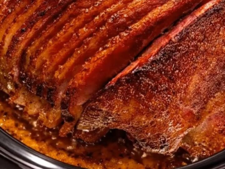 A beautifully caramelized spiral-cut ham glistening with sweet brown sugar glaze inside a black slow cooker
